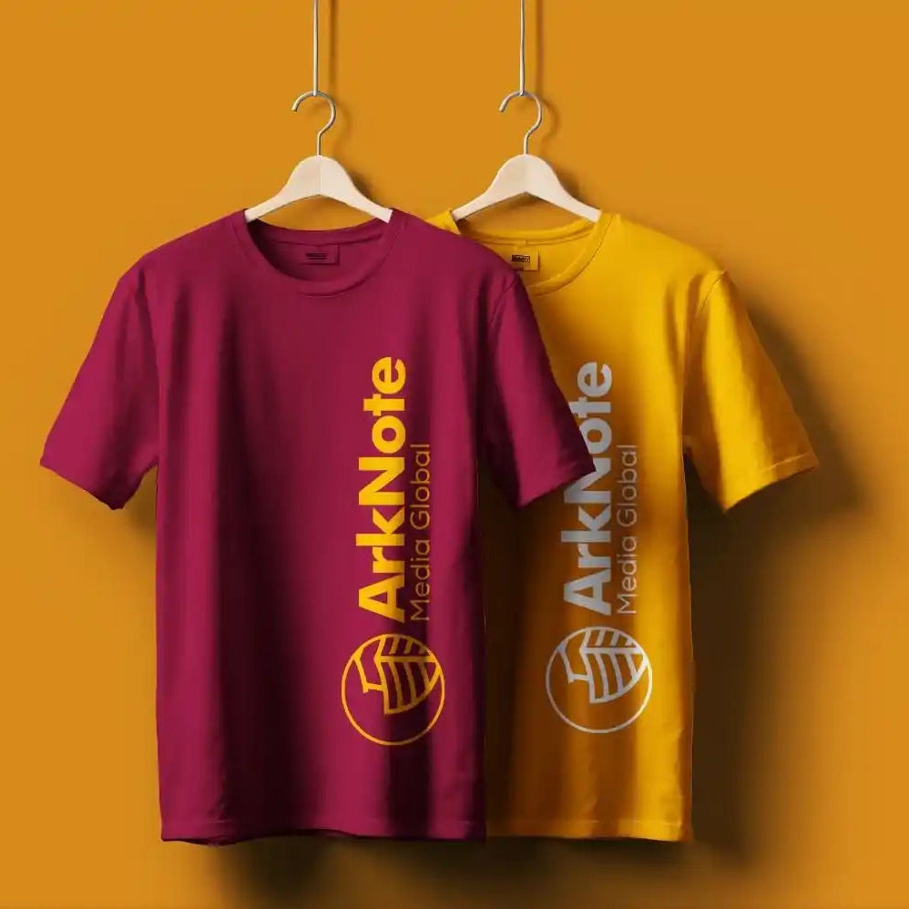 Two t-shirts, one purple and one yellow, with 'ArkNote Media Global' logos on a mustard yellow background.